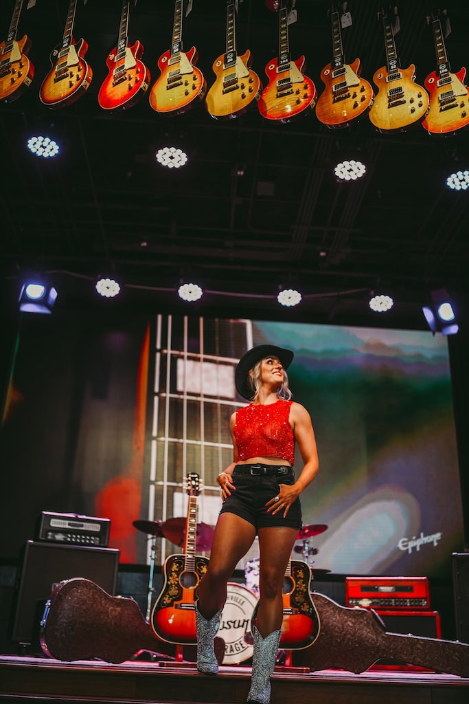 Photo of a girl on stage with guitars above her at Gibson Garage Nashville during a musician photoshoot