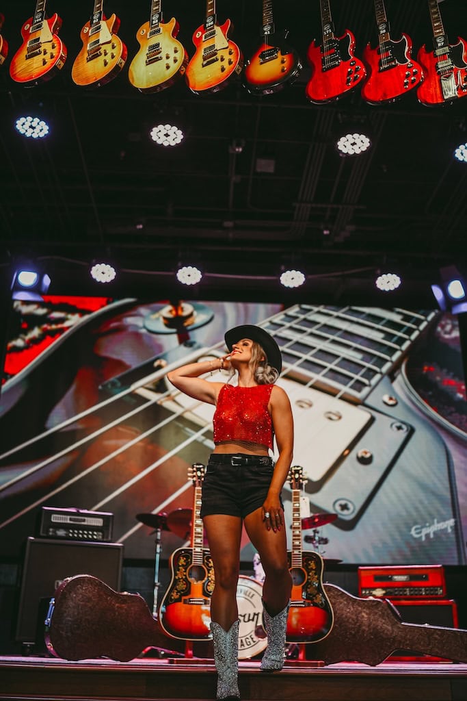 Photo of a girl on stage with guitars above her at Gibson Garage Nashville during a musician photoshoot